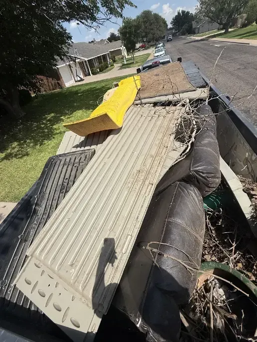 Dumpster filled with debris, including a yellow ramp and a tan radiator.
