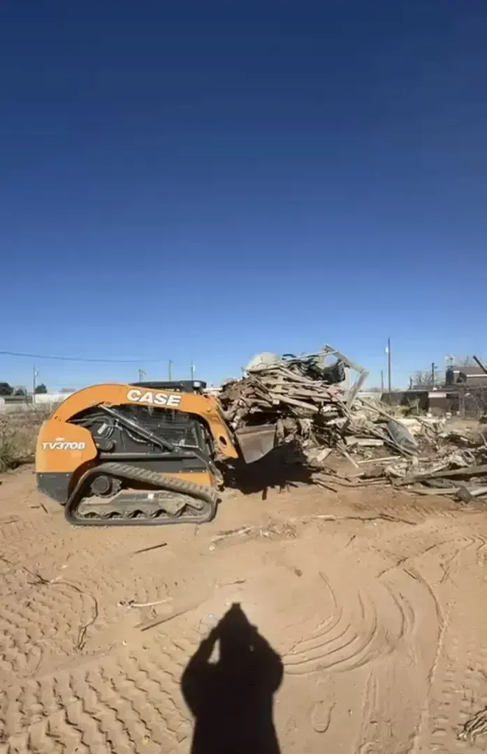 Orange Case skid steer removing debris under a clear blue sky.