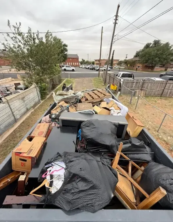 Boat filled with trash, cardboard boxes, and debris. Outdoors, overcast sky, street and buildings in background.
