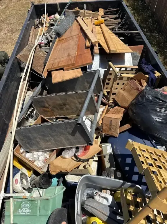 A dumpster filled with various debris, including wood, metal, and miscellaneous items.