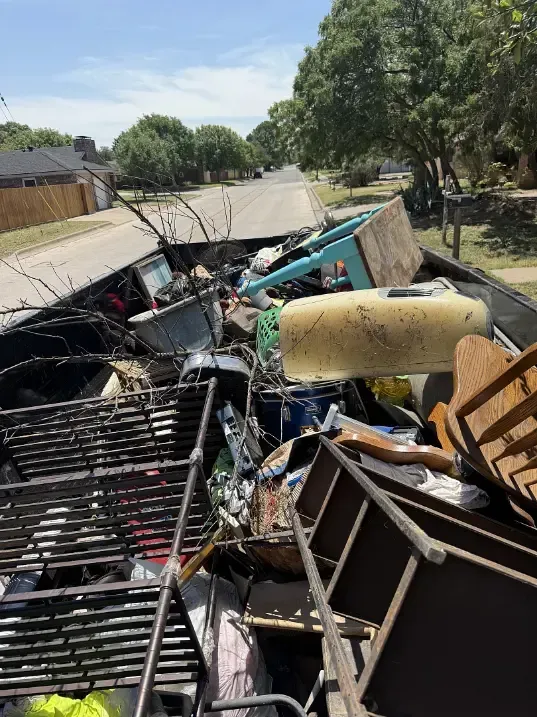 Truck bed overflowing with various discarded items, parked on a suburban street.