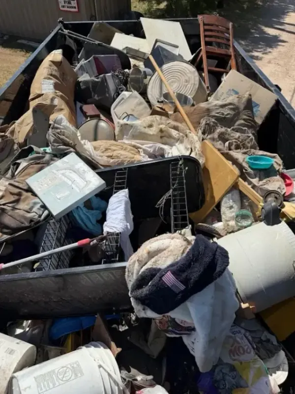 A dumpster overflowing with various debris, including furniture, building materials, and clothing.