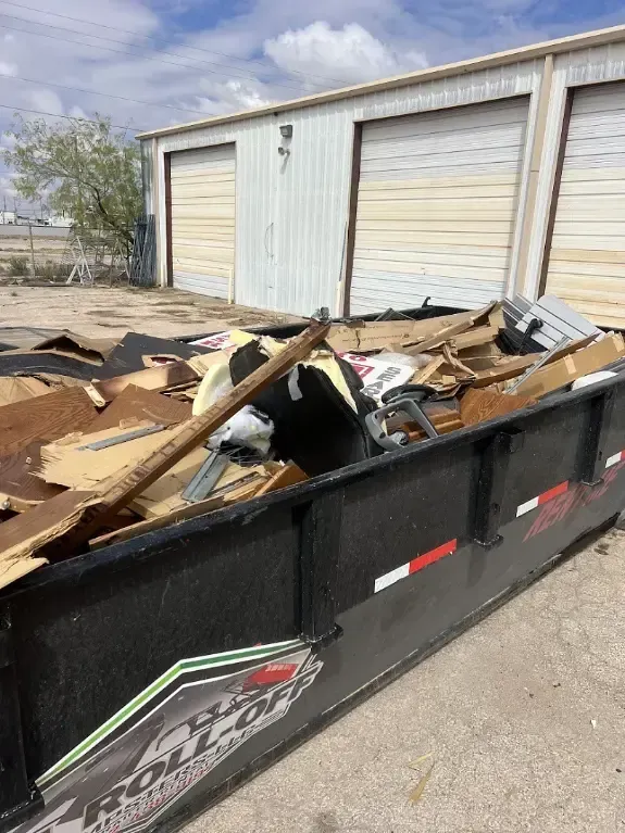 A black dumpster filled with construction debris sits in front of a white garage.