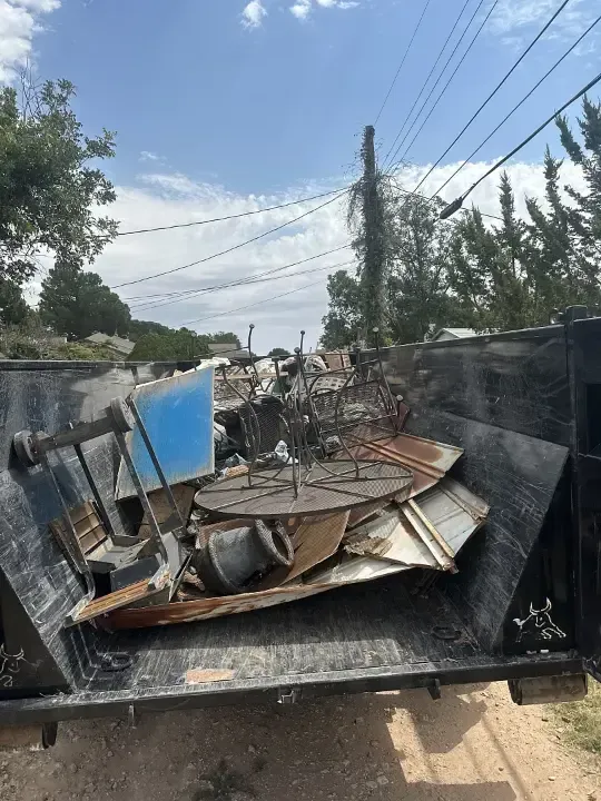 Dumpster filled with scrap metal and debris; blue sky and power lines in background.
