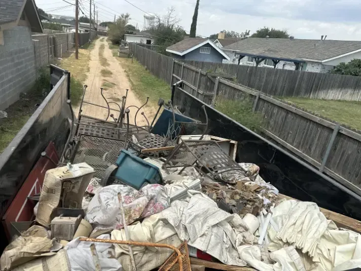 Dumpster filled with debris; alley in background with houses and fences.