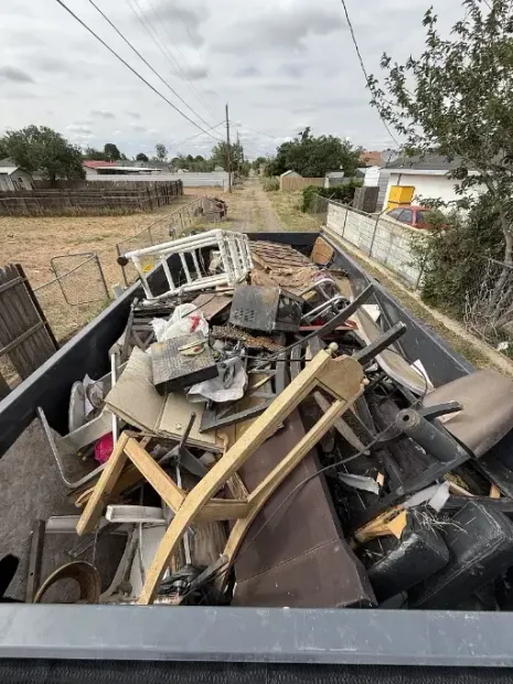 Truck bed filled with debris, including furniture and construction scraps, outdoors on a dirt road.