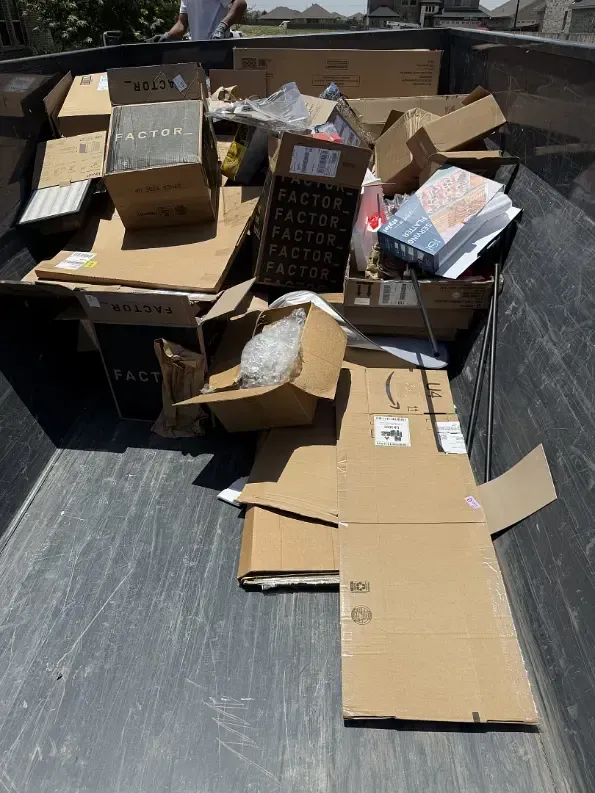 Cardboard boxes in a dumpster, various sizes and brands, viewed from above.