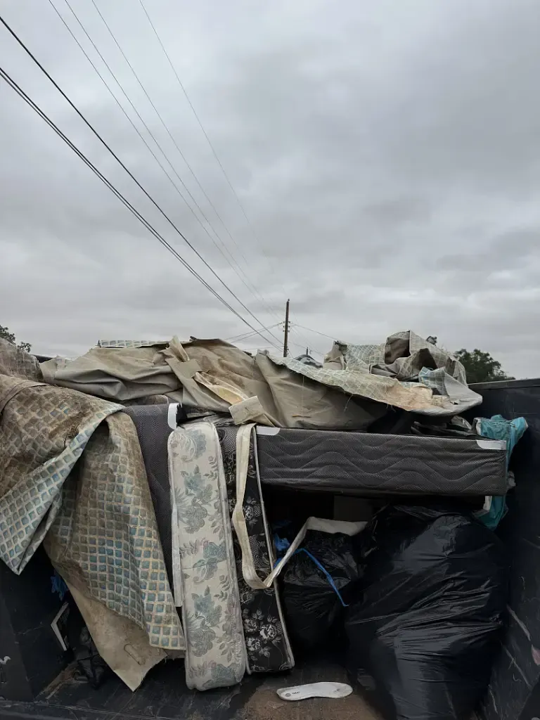 Truck bed filled with discarded furniture and trash beneath a cloudy sky.