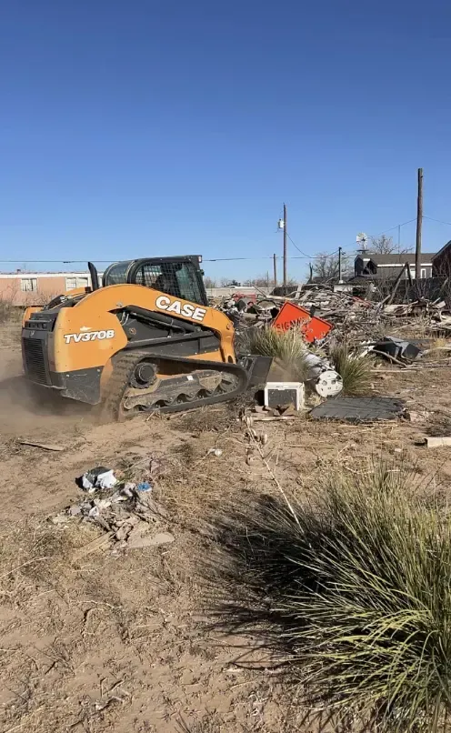 A Case skid steer clears debris from a building under clear blue skies.