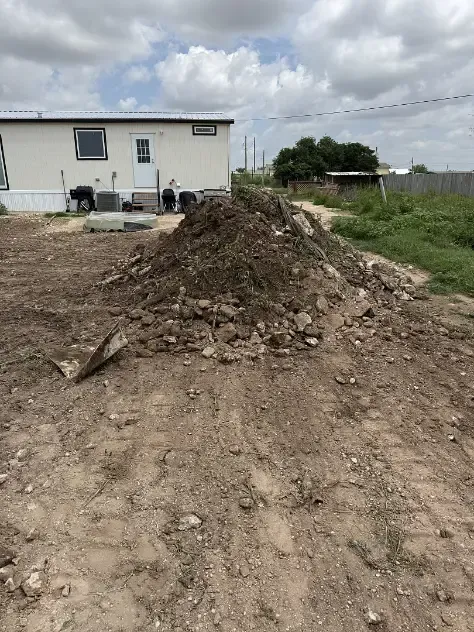 Pile of dirt in front of a white building with overcast sky.