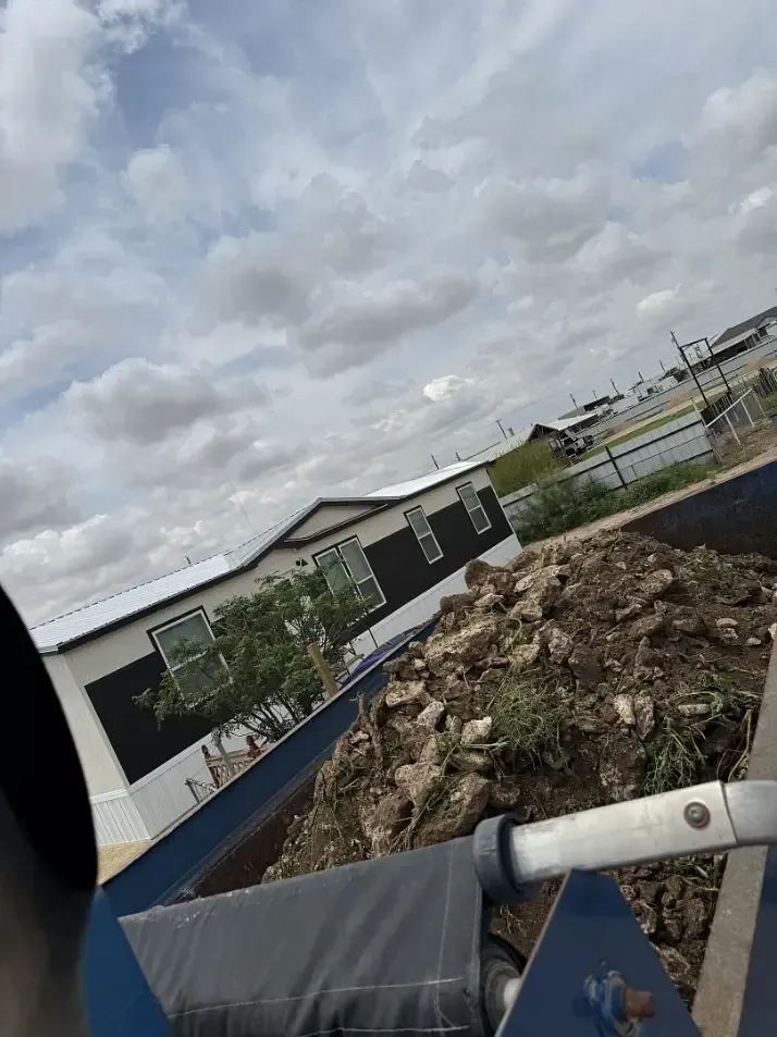 View from a vehicle towards a mobile home and pile of dirt under a cloudy sky.