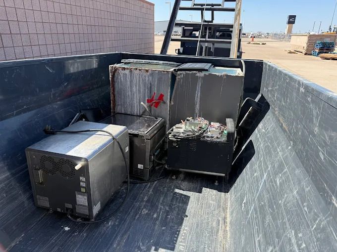 Several discarded appliances, including a microwave and a refrigerator, in a large, dark container.
