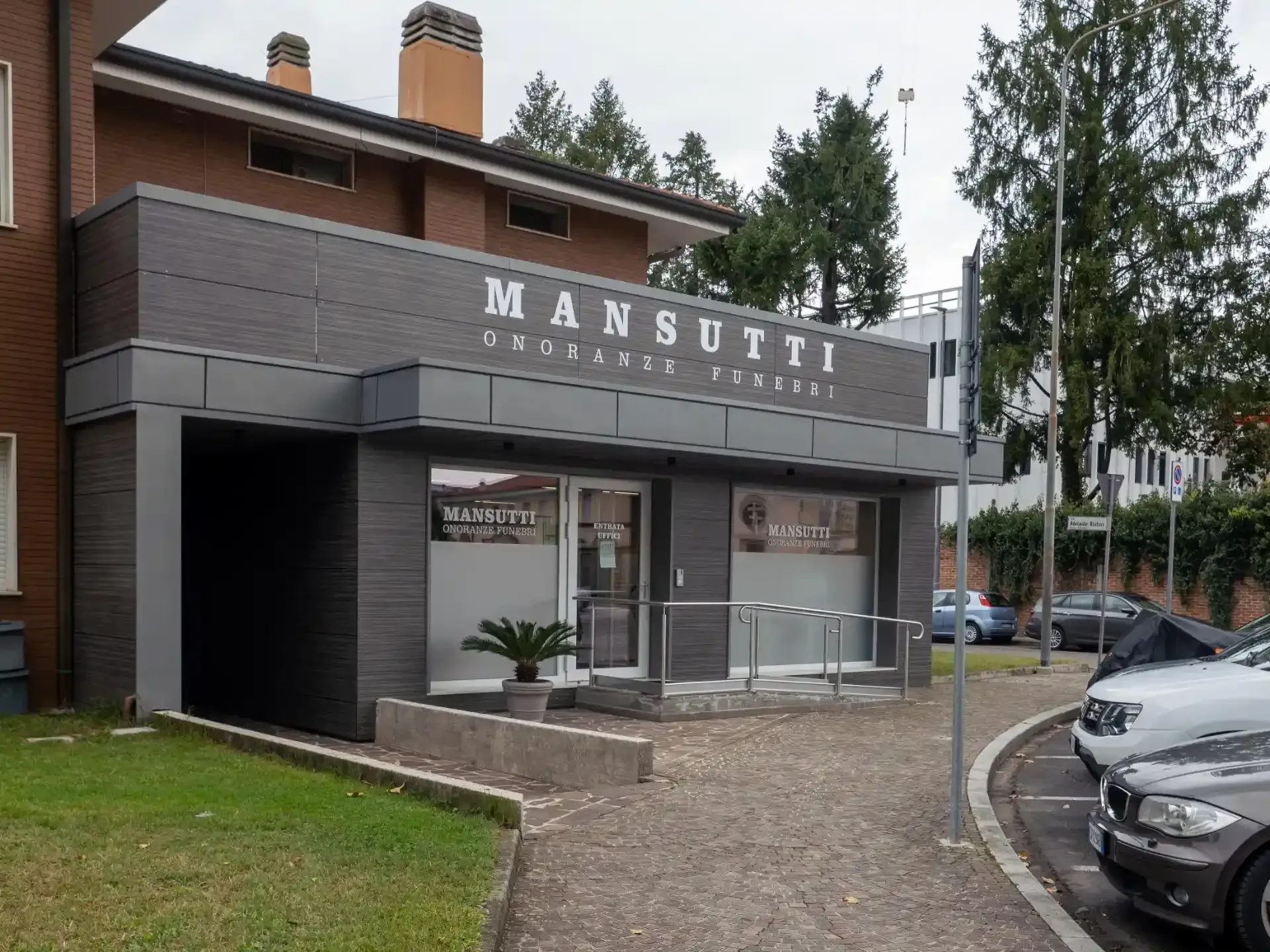 Esterno del negozio di uniformi Mansutti con facciata scura, segnaletica e auto parcheggiate.