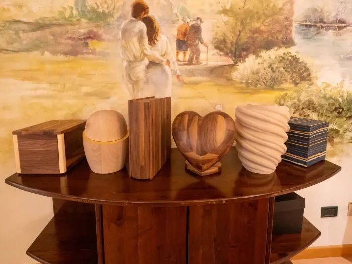 Urne di legno di varie forme e dimensioni su un tavolo di legno scuro, con un murale sullo sfondo.