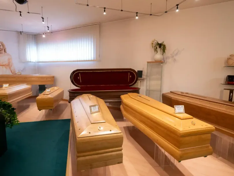 Interno di un'agenzia di pompe funebri con esposte diverse bare di legno.