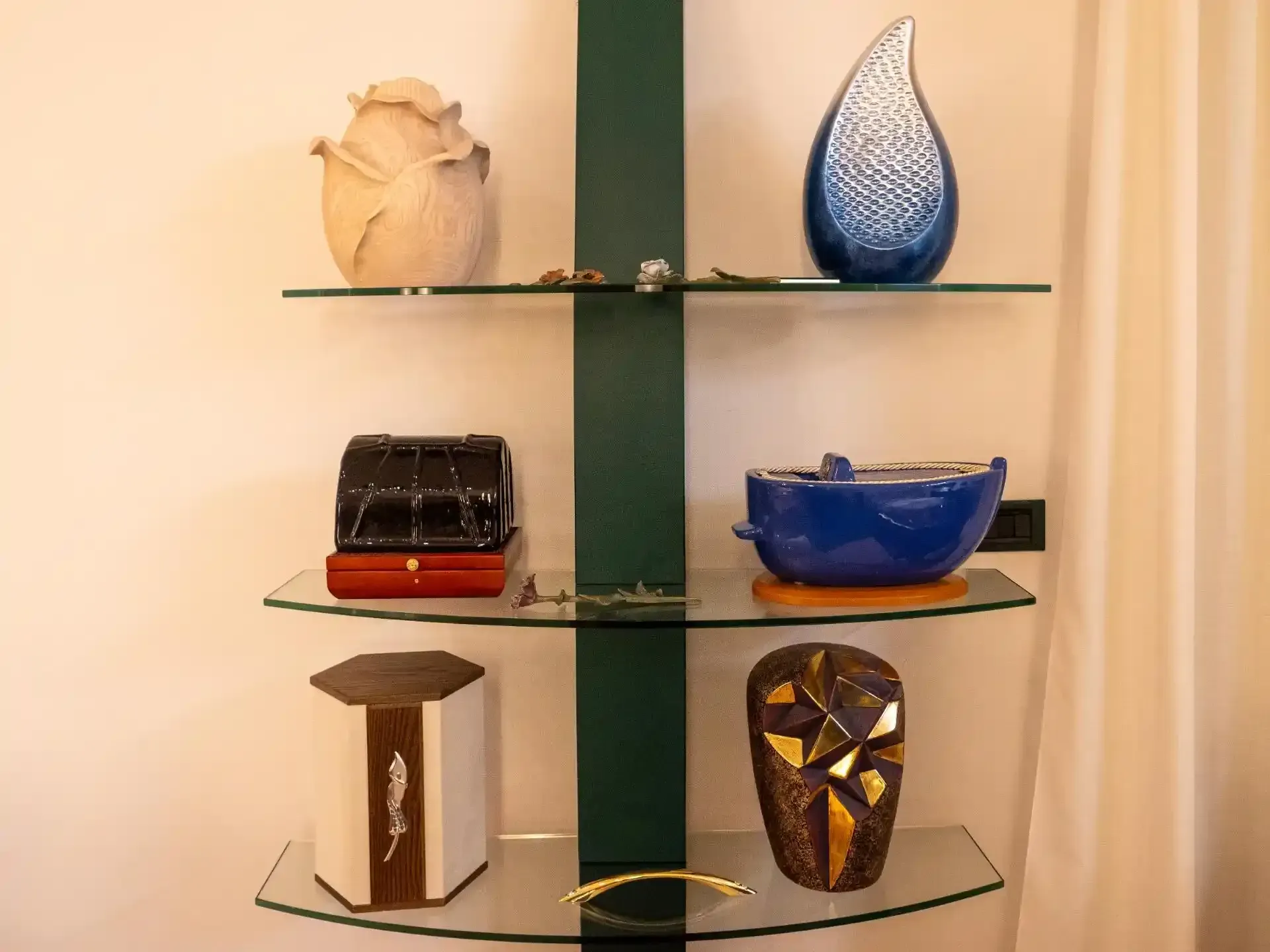 Mensole in vetro su cui sono esposti vasi e scatole decorative, contro una parete bianca e una tenda.