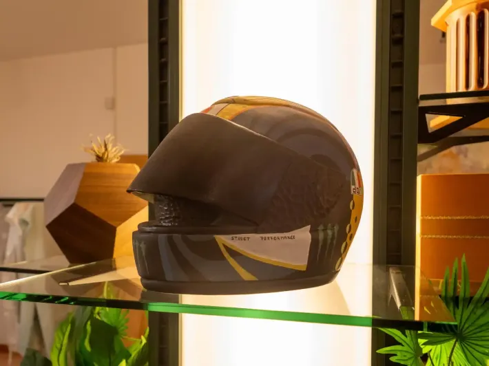 Casco da motociclista nero e oro su una mensola di vetro, con visiera scura.