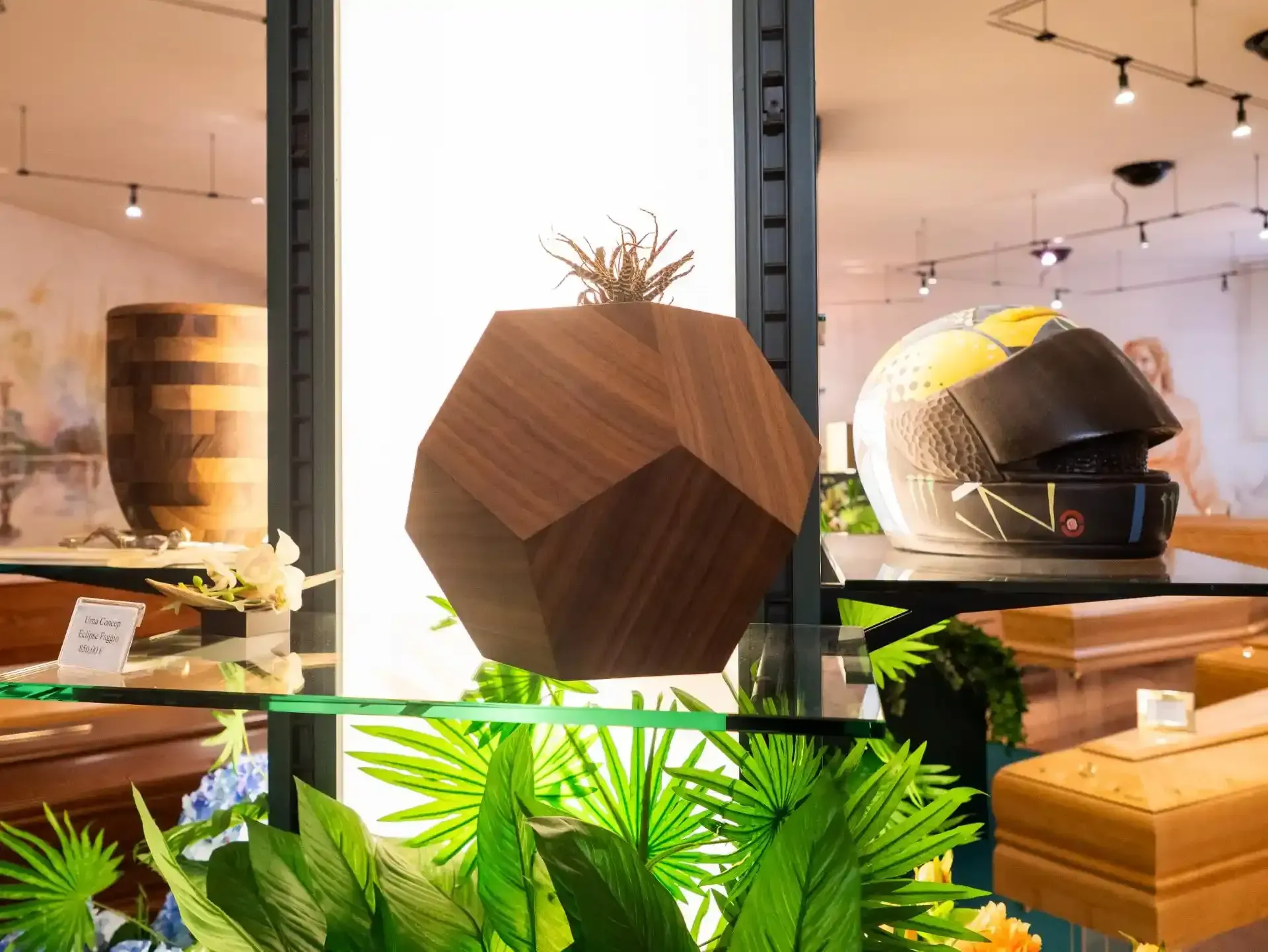 Urna in legno con decorazioni vegetali, casco da motociclista e bare esposte in un negozio ben illuminato.