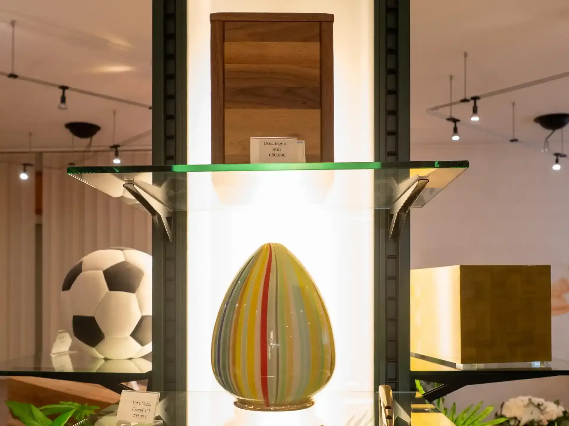 Vetrina con vari oggetti: pallone da calcio, uovo a strisce, scatola di legno e cubo d'oro.