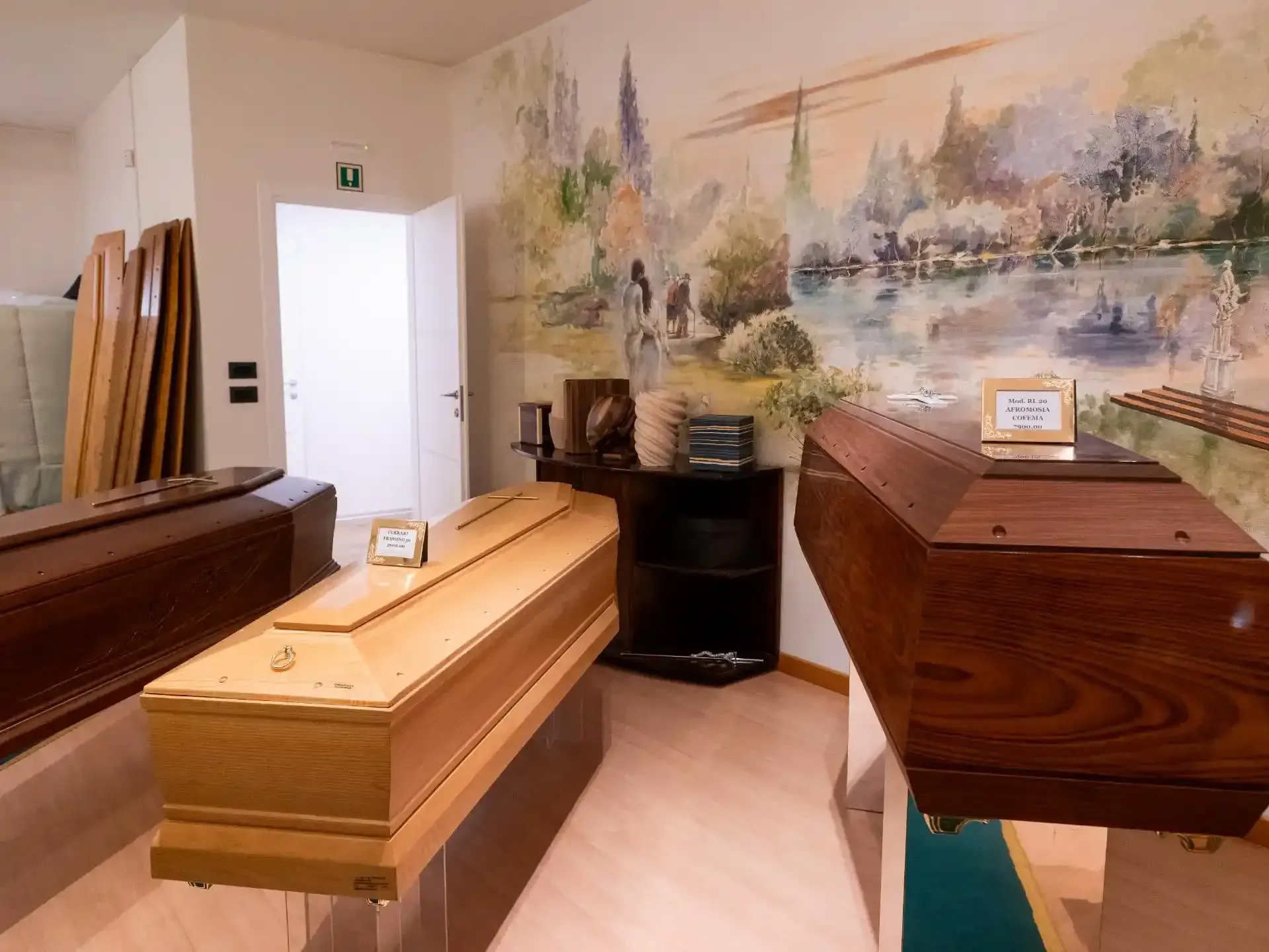 Sala espositiva di un'agenzia di pompe funebri con diverse bare in legno esposte; sullo sfondo un murale dipinto.