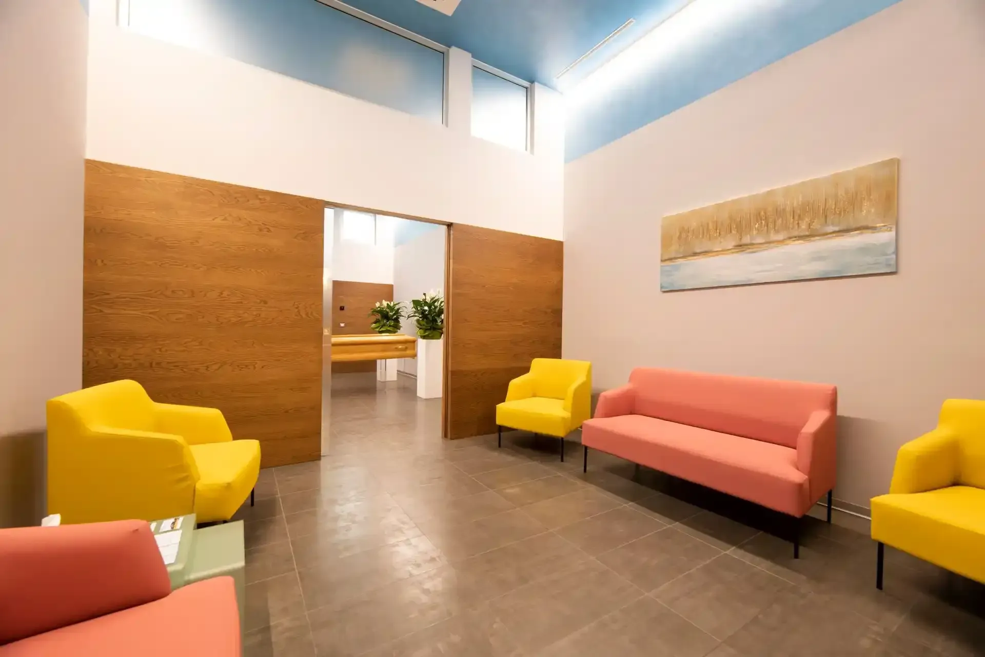 Sala d'attesa con mobili colorati, porte scorrevoli in legno e un dipinto.