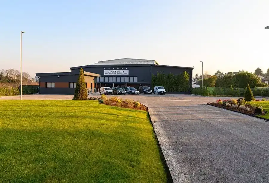 Edificio con facciata scura, auto parcheggiate, prato verde e un sentiero.