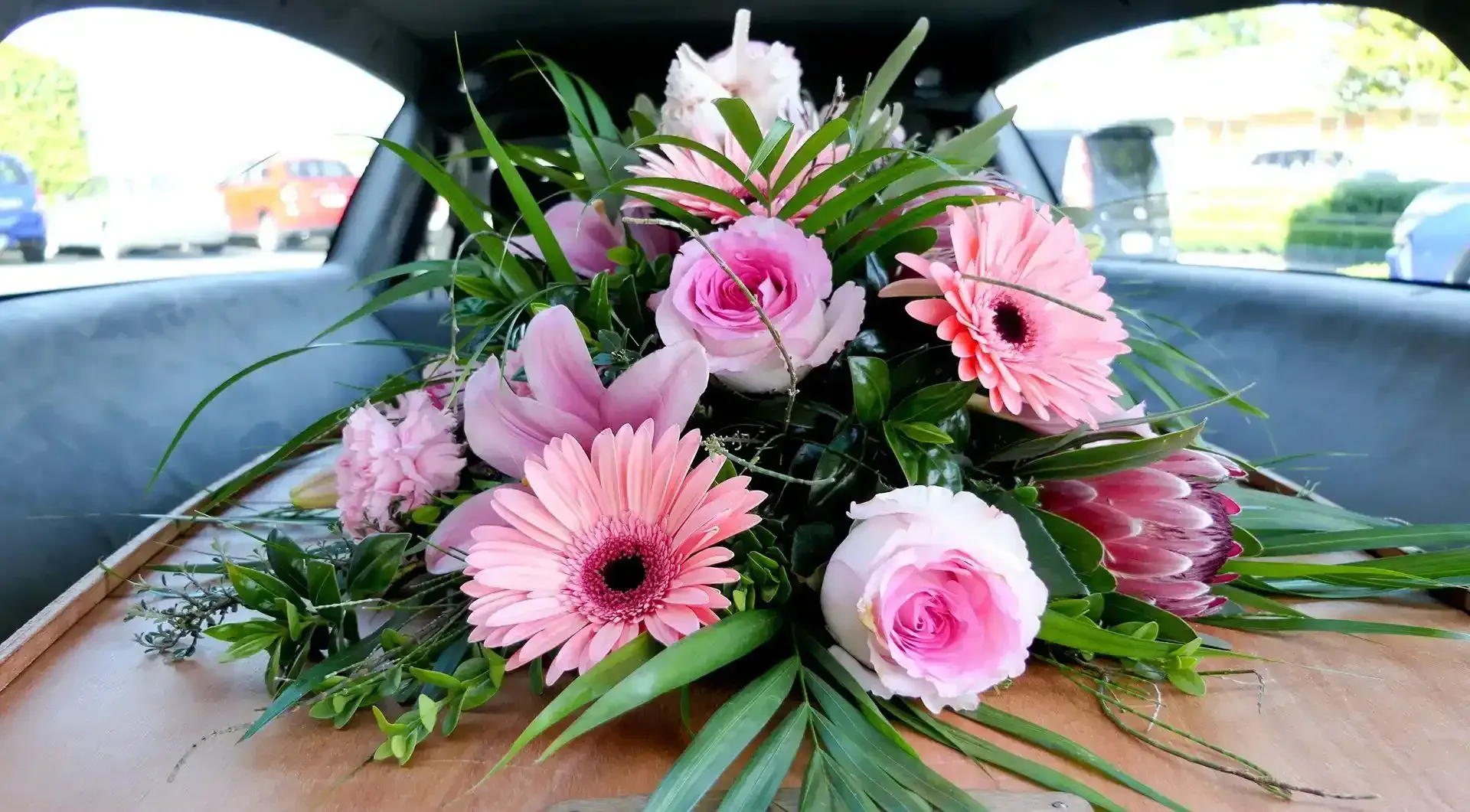 Fiori sopra una bara all'interno di un carro funebre, tra cui rose rosa e gerbere.