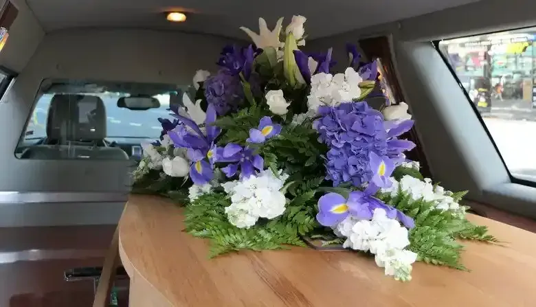 Composizione floreale su una bara all'interno di un carro funebre; fiori blu e bianchi.