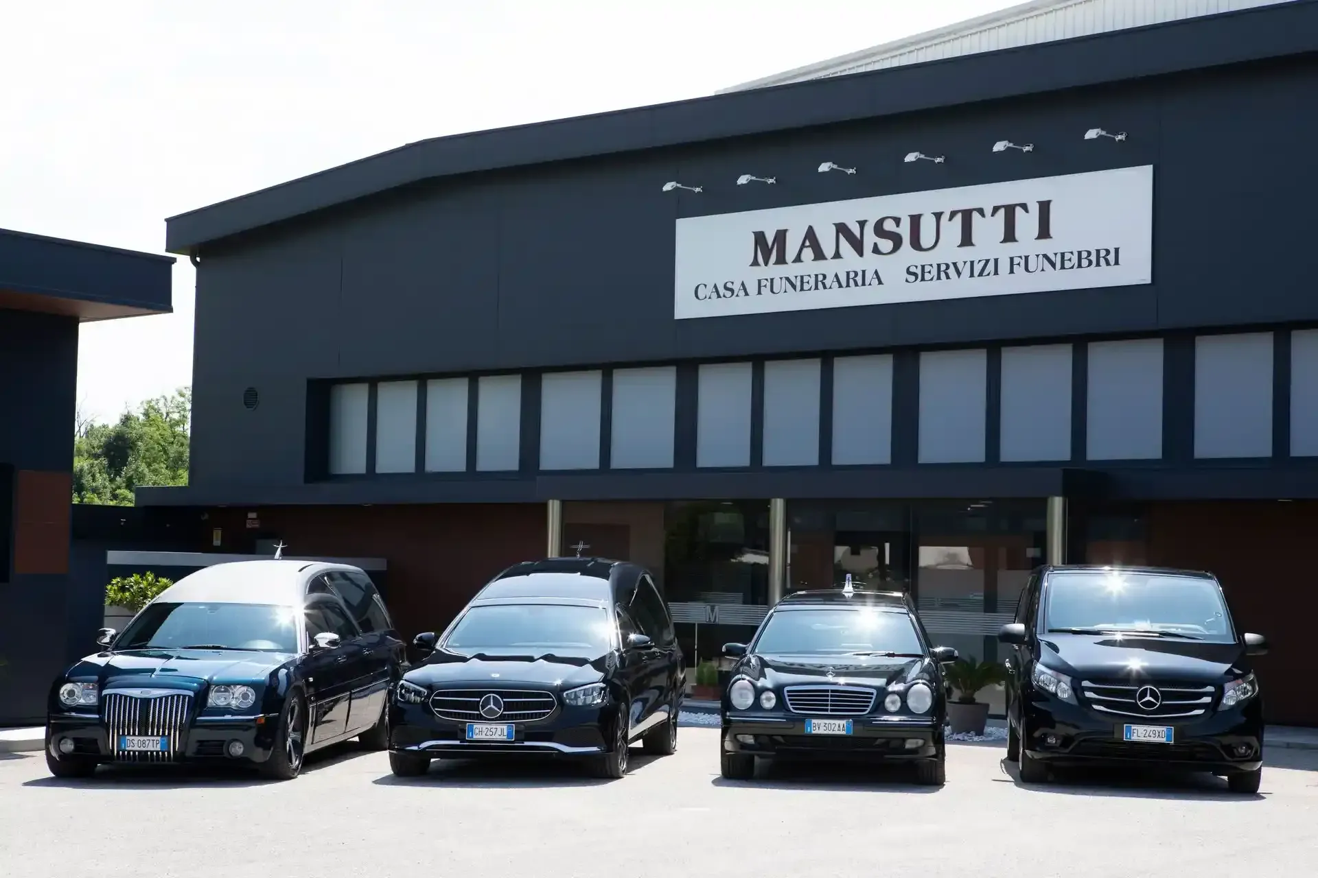 Carri funebri neri parcheggiati davanti a un'agenzia di pompe funebri con la scritta