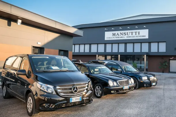 Tre carri funebri neri parcheggiati davanti a un edificio con la scritta 