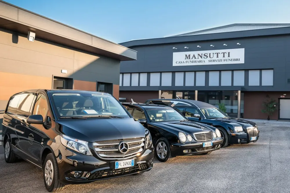Tre carri funebri neri parcheggiati davanti ad un edificio con la scritta 