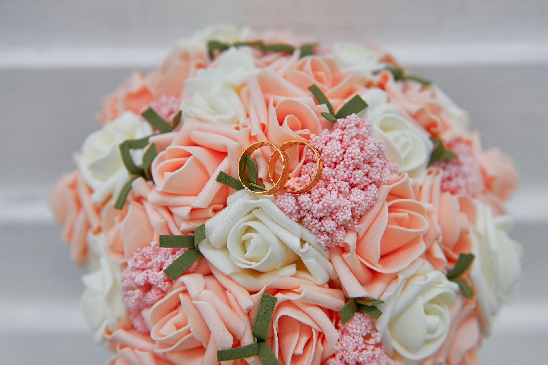 Peach and white rose bouquet with wedding rings and small pink flowers.