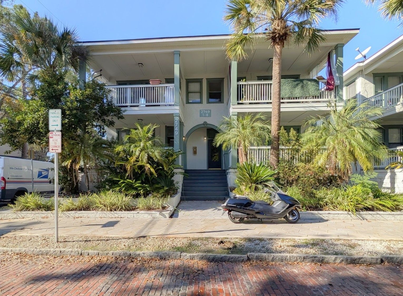 Two-story apartment building with stairs leading to a front door. A scooter is parked in front.