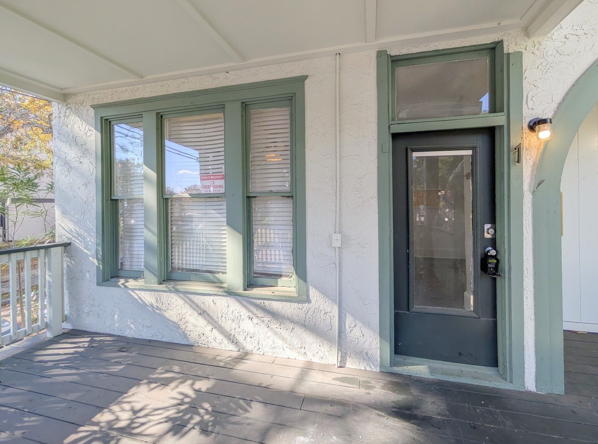 Covered porch with green-trimmed windows and door on a stucco exterior.