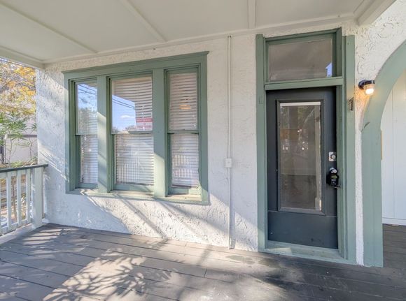 Covered porch with green-trimmed windows and door on a stucco exterior.