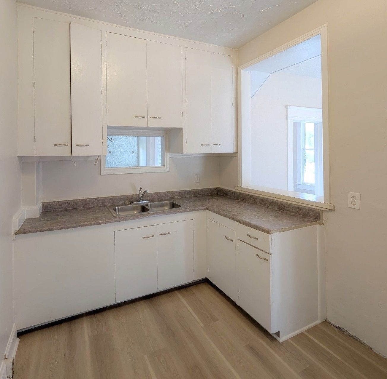 White kitchen with cabinets, countertops, sink, and a pass-through window.