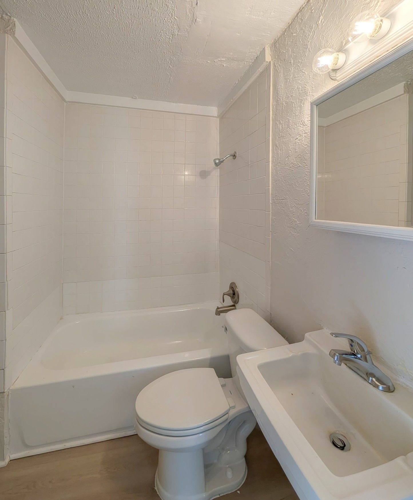 Small white bathroom with a tub, toilet, sink, and mirror.