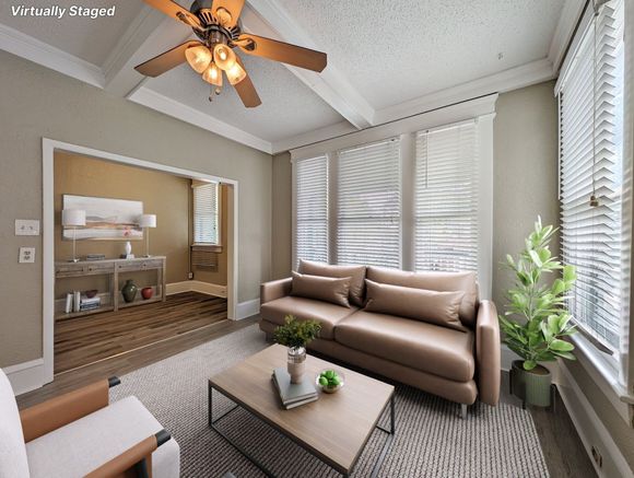 Living room with tan sofa, coffee table, rug, and windows with blinds.