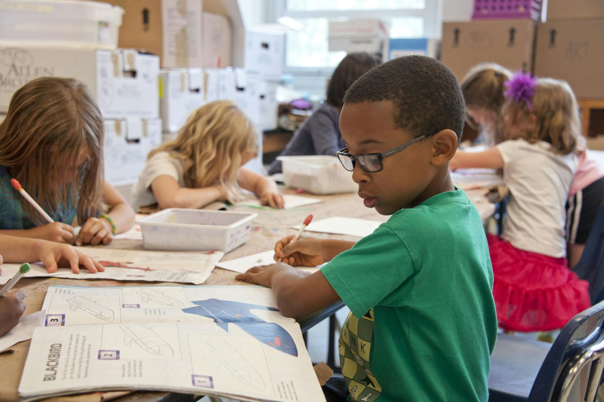 Children in a classroom writing at desks, focused on their work.
