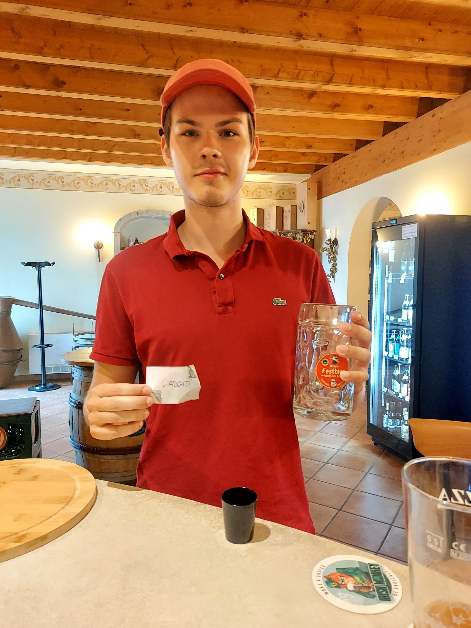 Un uomo con una camicia rossa tiene in mano una tazza di caffè e un bicchiere di birra.