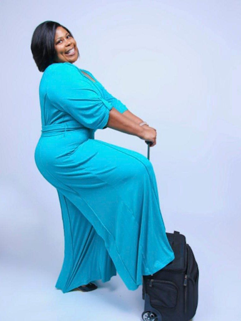 Side Profile Of A Black Woman Smiling At The Camera While Holding A Suitcase