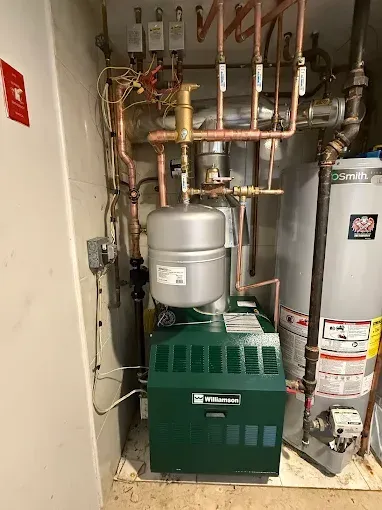 A green residential boiler and water heater with copper pipes in a utility room.