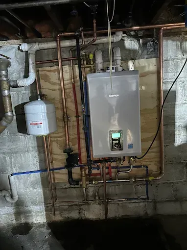 Tankless water heater with copper pipes and expansion tank in a basement.