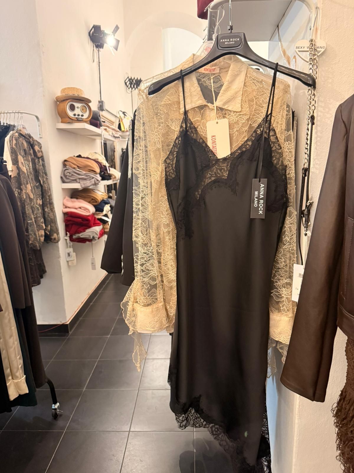 Abito sottoveste nero con finiture in pizzo e camicia marrone chiaro appesi in un negozio di abbigliamento.
