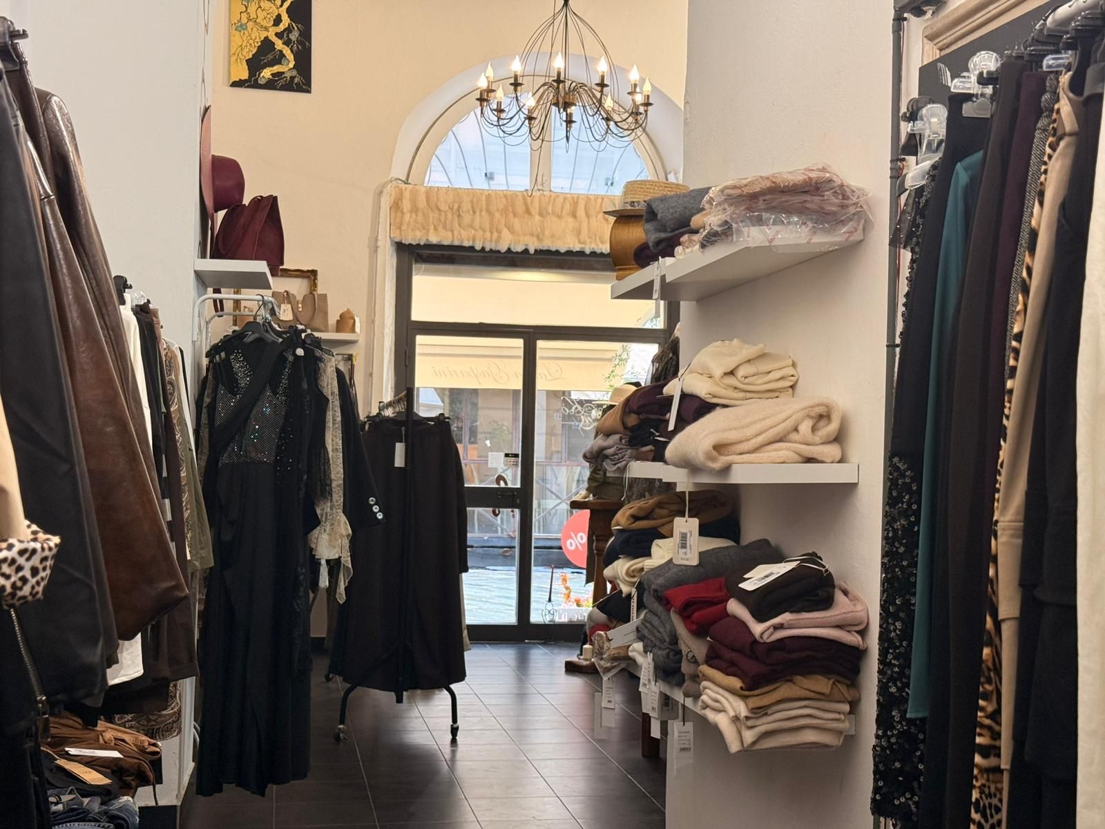 Interno di un negozio di abbigliamento con scaffali pieni di indumenti, scaffali con articoli piegati e una porta ad arco.