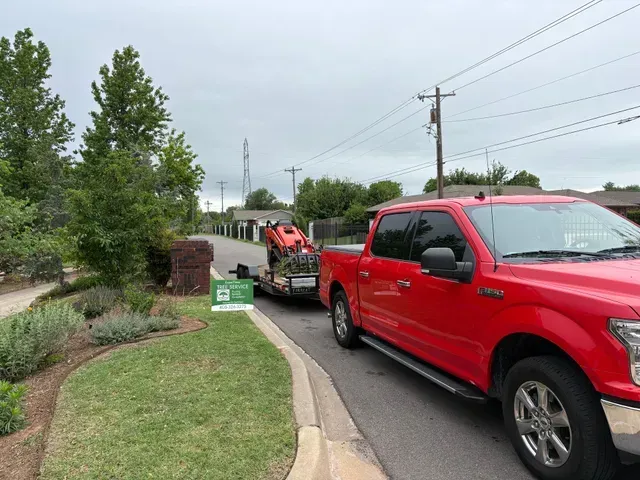 Red pickup truck parked on a curved street beside a utility vehicle and sidewalk in a suburban neighborhood