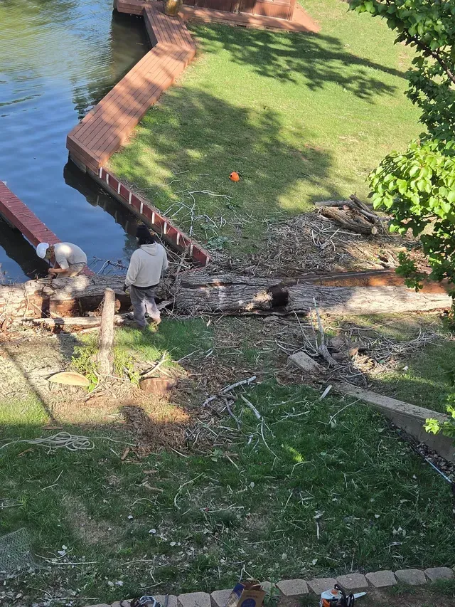Two workers clearing storm debris beside a brick-lined canal and grassy bank