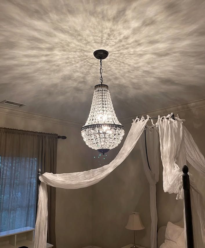 Crystal chandelier in a bedroom with draped white sheer fabric and curtains near a window.