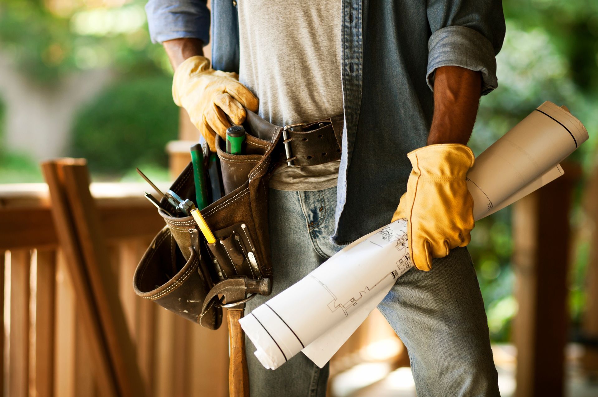 Home addition remodeling contractor with blueprints and tool belt on construction site.