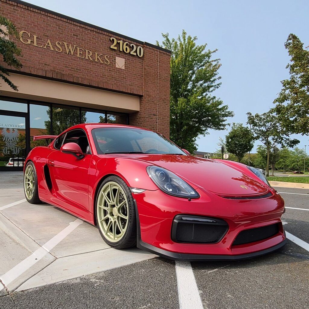 A red sports car is parked in front of a glassworks building.